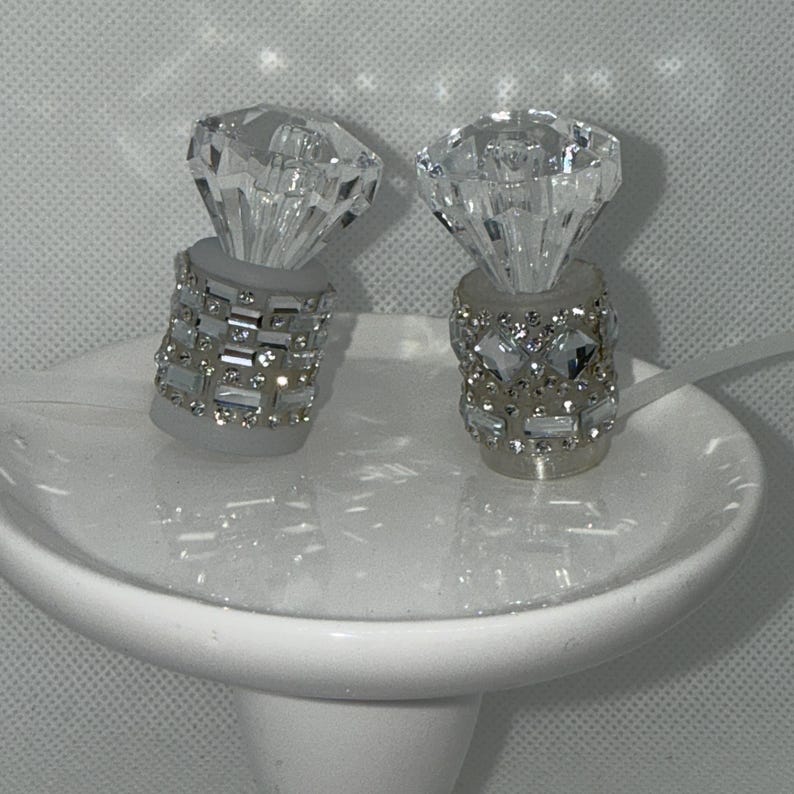 May include: Two clear glass bottle stoppers with a diamond shape on top and a silver base with rhinestones.