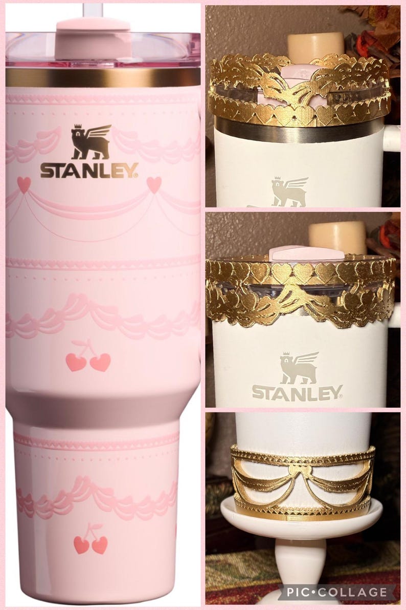 May include: Pink Stanley tumbler with a decorative design featuring cherries and hearts. The tumbler has a straw and a lid. The Stanley logo is visible. The image also shows a white mug with gold decorative bands.