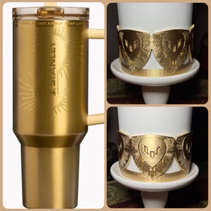May include: A gold-colored Stanley travel mug with a handle and a clear lid. The mug has the Stanley logo and the text "START EARLY - STAY LATE". Also shown are gold-colored decorative bands around a white mug.