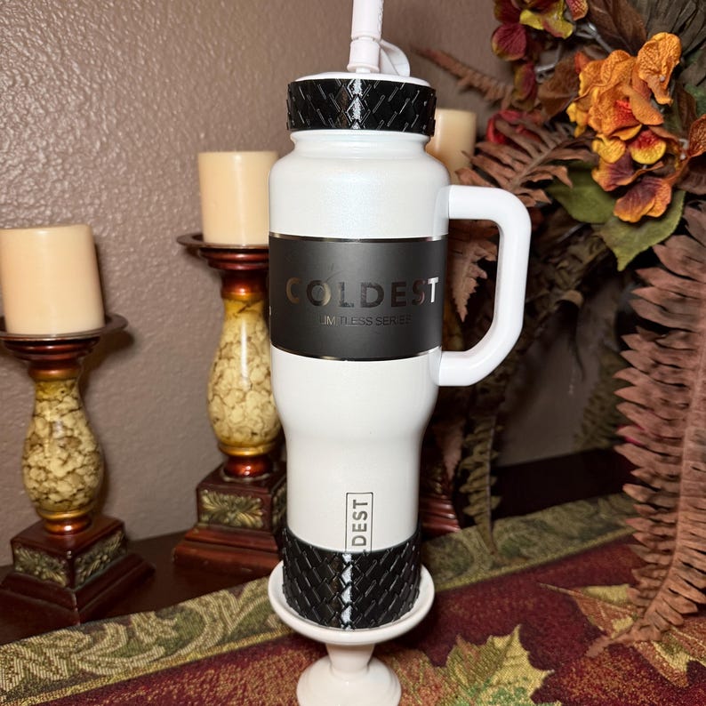 May include: White insulated water bottle with a black band featuring the word "COLDEST" and "LIMITLESS SERIES". The bottle has a white handle and a black textured top and bottom. A white straw extends from the top.