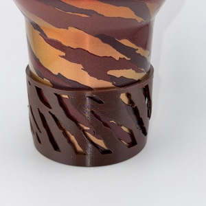 May include: A brown and gold patterned cup with a brown plastic ring around the bottom. The ring has a cut-out design.