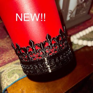 May include: A red tumbler with a black lace trim around the top. The tumbler has the word "NEW!" written on the side.