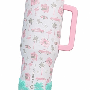 May include: A white tumbler with a pink handle and lid, featuring a repeating pattern of pink flamingos, palm trees, vintage cars, suitcases, umbrellas, and hotel signs. The base has a textured mint green silicone sleeve with palm tree motifs.