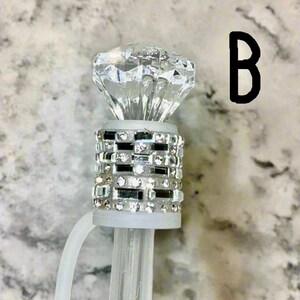 May include: A clear plastic diamond-shaped topper with a silver and clear rhinestone band. The topper is attached to a clear plastic stick.