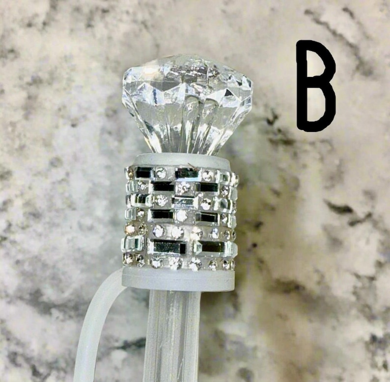 May include: A clear plastic diamond-shaped topper with a silver and clear rhinestone band. The topper is attached to a clear plastic stick.