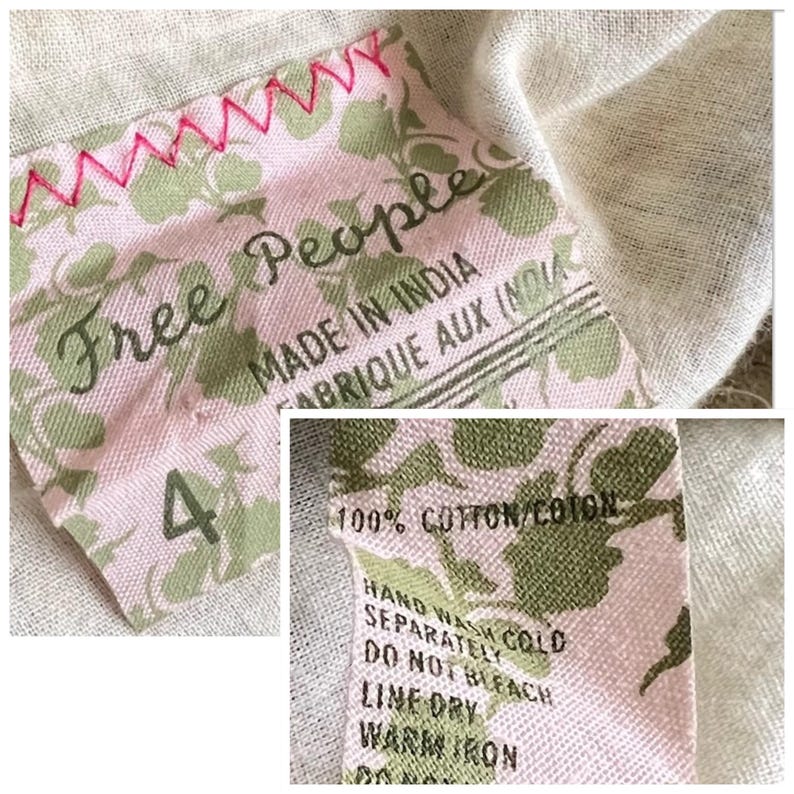 以下が含まれることがあります： 「Free People」と「Made in India」の文字が入ったピンクとグリーンの布製タグのクローズアップ。タグには花柄模様があり、ピンクの糸で縫われています。「4」の数字が見えます。