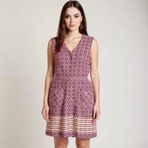 May include: A sleeveless, knee-length dress with a V-neck and a geometric pattern in shades of purple, pink, and beige. The dress features a button-down front, a fitted waist, and two front pockets. The hemline has a decorative border.