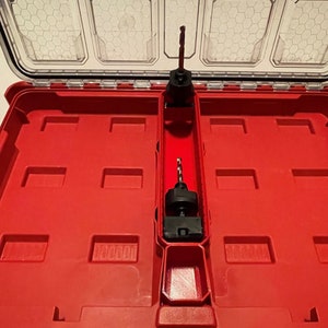 May include: A red plastic tool case with a black drill bit and a black tool inside. The case has a handle and a latch.