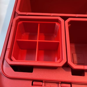 Może przedstawiać: Czerwony plastikowy organizer do przechowywania z wieloma przegródkami. Organizer ma siatkę czterech mniejszych przegródek w ramach większej przegródki.