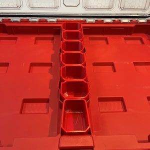 Puede incluir: Caja de herramientas de plástico roja con una bandeja extraíble que contiene varios compartimentos. La bandeja está diseñada para contener artículos pequeños como tornillos, tuercas y pernos.