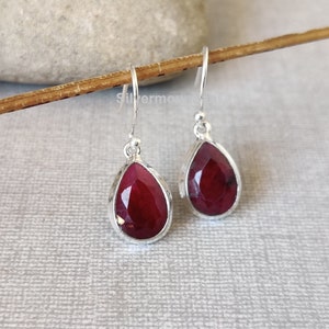 May include: A pair of silver dangle earrings with red teardrop-shaped gemstones.