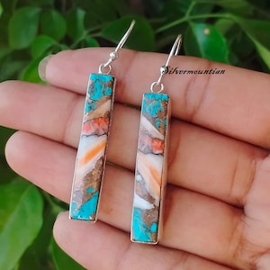 May include: A pair of silver dangle earrings with turquoise, brown, and white stone accents. The stones are arranged in a vertical pattern.