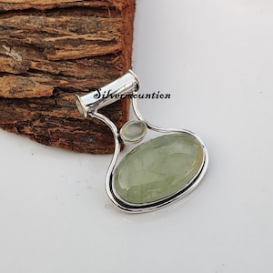 May include: A silver pendant featuring a green oval gemstone and a smaller round white gemstone. The pendant is shaped like a teardrop and has a silver bail.