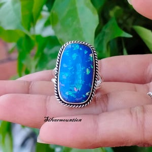 May include: A silver ring with a large blue opal gemstone. The opal has a unique iridescent pattern with hints of green and pink.