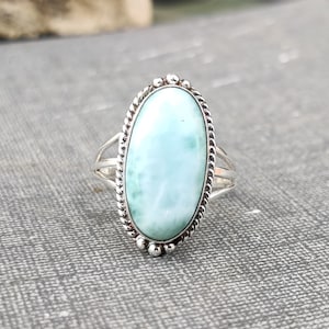 May include: A silver ring featuring a light blue oval-shaped gemstone set in a twisted silver band.