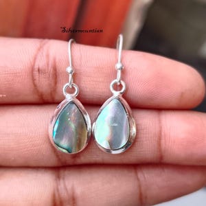 May include: A pair of silver teardrop earrings with iridescent abalone shell inlays.