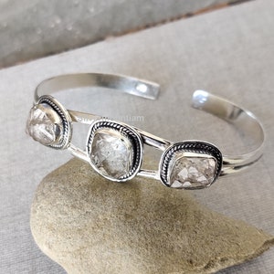 May include: Silver bangle bracelet with three clear, faceted, square-shaped stones set in silver.