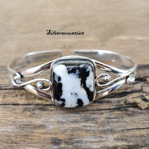 May include: Silver cuff bracelet with a black and white stone set in a silver bezel. The bracelet has a delicate, twisted design.