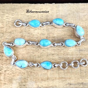 May include: A silver chain bracelet with light blue teardrop-shaped stones. The bracelet has a lobster claw clasp.