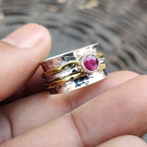 May include: A silver and gold spinner ring with a red gemstone. The ring is hammered and has a textured finish.