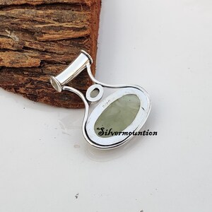 May include: A silver pendant featuring a green stone set in an oval shape. The pendant has a bail at the top and the words "Silvermounton" are engraved on the back.