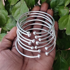 May include: A set of seven silver bangles with small round beads at the ends. The bangles are stacked on top of each other.