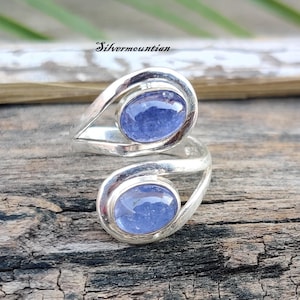 May include: A silver ring with two oval-shaped blue gemstones. The ring is designed with a twisted band and the gemstones are set in a bezel setting.
