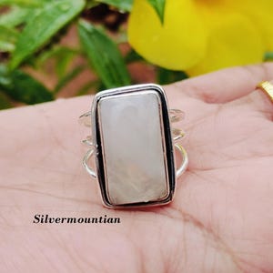 May include: A silver ring with a white rectangular gemstone. The ring has a delicate, intricate design.