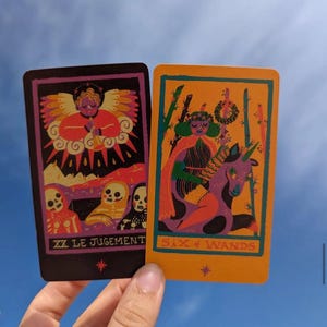 May include: Two tarot cards are displayed against a blue sky. One card is black with a purple border and features an angel and skeletons. The other card is orange with a green border and depicts a person riding a purple unicorn. The text "XX LE JUGEMENT" and "SIX of WANDS" are visible.