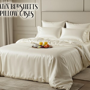 Könnte beinhalten: Elfenbeinfarbene Satin-Bettwäsche und Kissenbezüge auf einem Bett. Das Bett ist mit einem Bettbezug und mehreren Kissen ausgestattet. Ein Tablett mit Obst und Getränken steht auf dem Bett. Der Text "SATIN BEDSHEETS PILLOW CASES" steht oben.