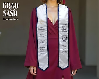 May include: White graduation sash with blue trim and black embroidery. The text on the sash reads "The Observer Social Media Editor", "Honor Roll X2", "Observer Civic Award 4x's", "Jabetha Latice Mastin Howard", "Class of 2024".