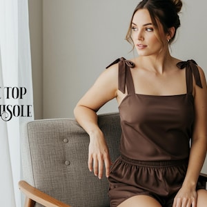Könnte beinhalten: Ein dunkelbraunes Camisole mit zum Binden gestalteten Schulterträgern und passender Shorts mit elastischem Bund. Der Text TIE TOP CAMISOLE ist links aufgedruckt. Das Kleidungsstück hat einen eckigen Ausschnitt und einen glatten Stoff.