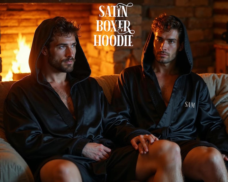 May include: Two people wearing black satin boxer hoodies with the word "SAM" embroidered on the left chest. The hoodies have attached hoods and are worn open. The image is set in front of a fireplace.