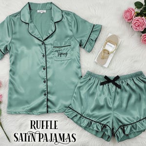 May include: A green satin pajama set with black trim and ruffles. The top has a button-up front and a pocket with the name "Tiffany" embroidered on it. The shorts have a bow at the waist.