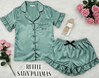 May include: A green satin pajama set with black trim and ruffles. The top has a button-up front and a pocket with the name "Tiffany" embroidered on it. The shorts have a bow at the waist.