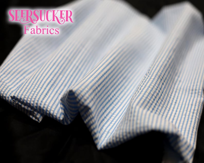 Puede incluir: Primer plano de tela seersucker con rayas azules y blancas. La tela est&aacute; doblada, mostrando la textura y el patr&oacute;n. El texto "SEERSUCKER Fabrics" est&aacute; en rosa en cursiva.