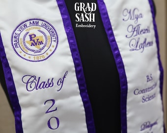 May include: White graduation sash with purple trim. The sash has the text "Prairie View A&M University" with a logo and the year "1876". The sash also has the text "Class of 20" and the name "Mya Alexis Lafleur" with the degree "BS Construction Science".