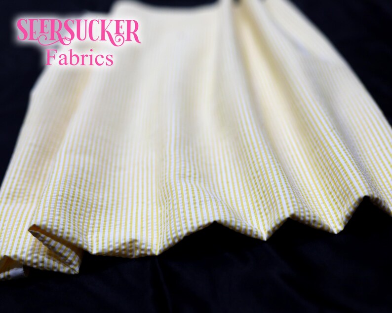 Puede incluir: Primer plano de tela seersucker con rayas verticales blancas y amarillo p&aacute;lido. La tela est&aacute; fruncida, mostrando un borde festoneado. El texto "SEERSUCKER Fabrics" es visible en rosa.