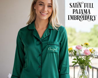 May include: A dark green satin pajama top with black piping along the collar, button placket, and cuffs. The shirt features a chest pocket embroidered with the name Angel in white script. Text in the upper right corner reads SATIN FULL PAJAMA EMBROIDERY.
