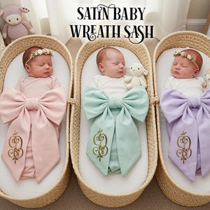 Puede incluir: Tres bebés en moisés tejidos, cada uno envuelto en una faja de satén. Las fajas son de color rosa pastel, verde menta y lavanda, con detalles bordados en dorado. La imagen incluye el texto "SATIN BABY WREATH SASH".