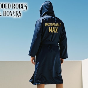 May include: A navy blue hooded robe with the text "UNSTOPPABLE MAX" in gold lettering on the back. The image also includes the text "HOODED ROBES & BOXERS" in the upper left corner.