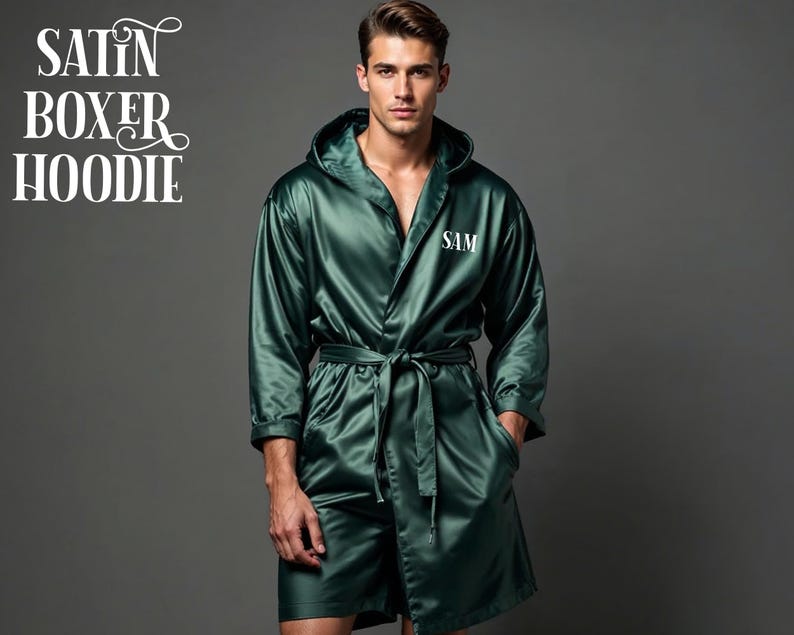 May include: A dark green satin boxer hoodie with a matching belt. The robe has a hood and the initials "SAM" are embroidered on the chest. The words "SATIN BOXER HOODIE" are in white script in the upper left corner.