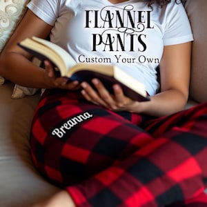May include: A person wearing red and black checked flannel trousers with the name "Breanna" embroidered on the left leg. The person is wearing a white t-shirt with the text "Flannel Pants Custom Your Own" printed on it.