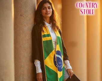 May include: A woman wearing a black graduation gown with a yellow and green sash featuring the Brazilian flag. The sash has the words "Ordem e Progresso" written on it. The text "COUNTRY STOLE" is visible in the background.