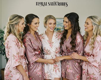 May include: Five women wearing floral print satin robes. The robes are in shades of pink and white. The women are smiling and looking at each other.
