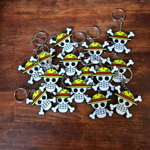 Puede incluir: Un conjunto de 15 llaveros con un cr&aacute;neo de dibujos animados con un sombrero de paja. Los llaveros est&aacute;n hechos de pl&aacute;stico y tienen una combinaci&oacute;n de colores amarillo y rojo.