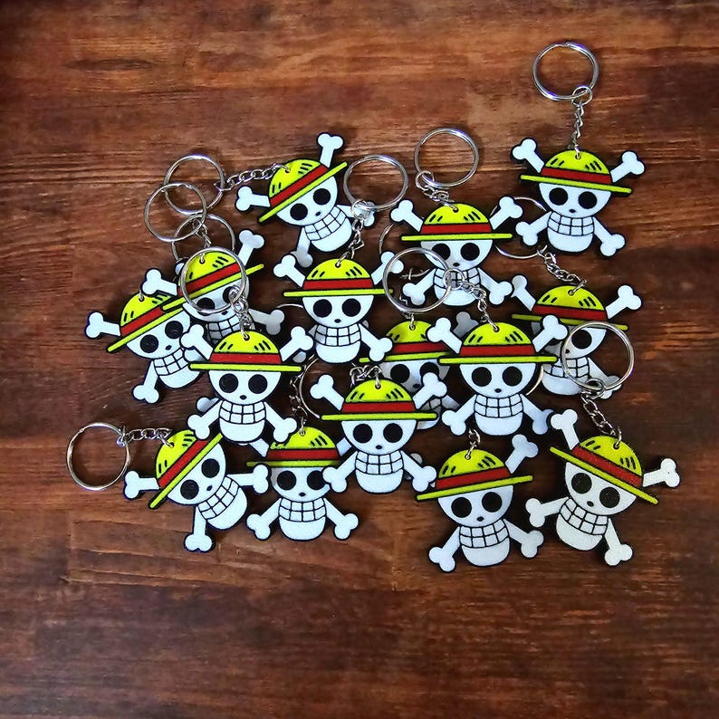 Puede incluir: Un conjunto de 15 llaveros con un cr&aacute;neo de dibujos animados con un sombrero de paja. Los llaveros est&aacute;n hechos de pl&aacute;stico y tienen una combinaci&oacute;n de colores amarillo y rojo.