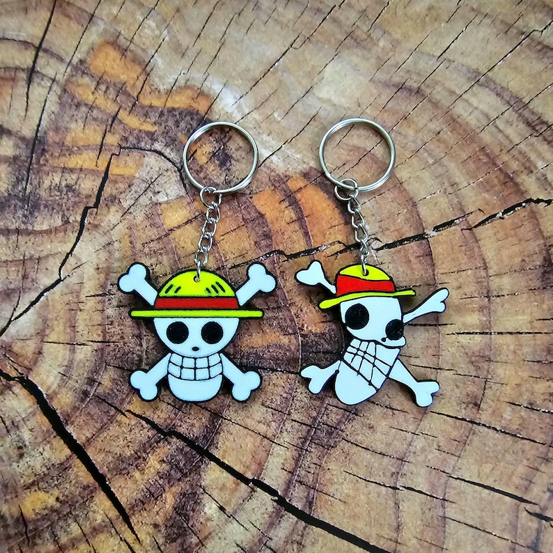Puede incluir: Dos llaveros con personajes de dibujos animados del anime One Piece. Los llaveros est&aacute;n hechos de pl&aacute;stico y presentan los sombreros y el dise&ntilde;o de calavera y huesos cruzados caracter&iacute;sticos de los personajes. Los llaveros est&aacute;n unidos a llaveros de plata.