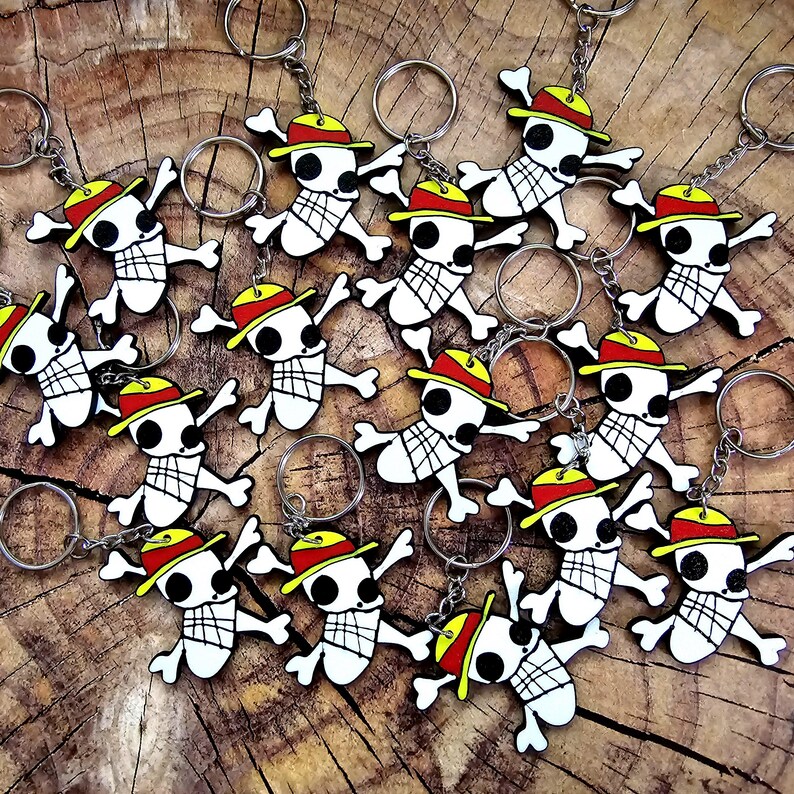 Puede incluir: Una colecci&oacute;n de 15 llaveros coloridos de calavera y huesos cruzados con detalles en amarillo, rojo y blanco. Cada llavero presenta una calavera de dibujos animados que lleva un sombrero rojo y amarillo.