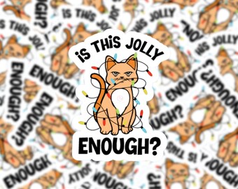 May include: A white sticker featuring a cartoon orange cat entangled in Christmas lights. The cat has a grumpy expression and the text reads "Is this jolly enough?"